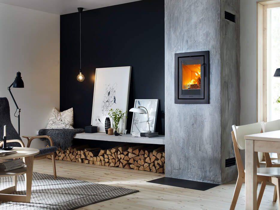 Wall-mounted wood burning stove set into a grey chimney breast beside stacked logs